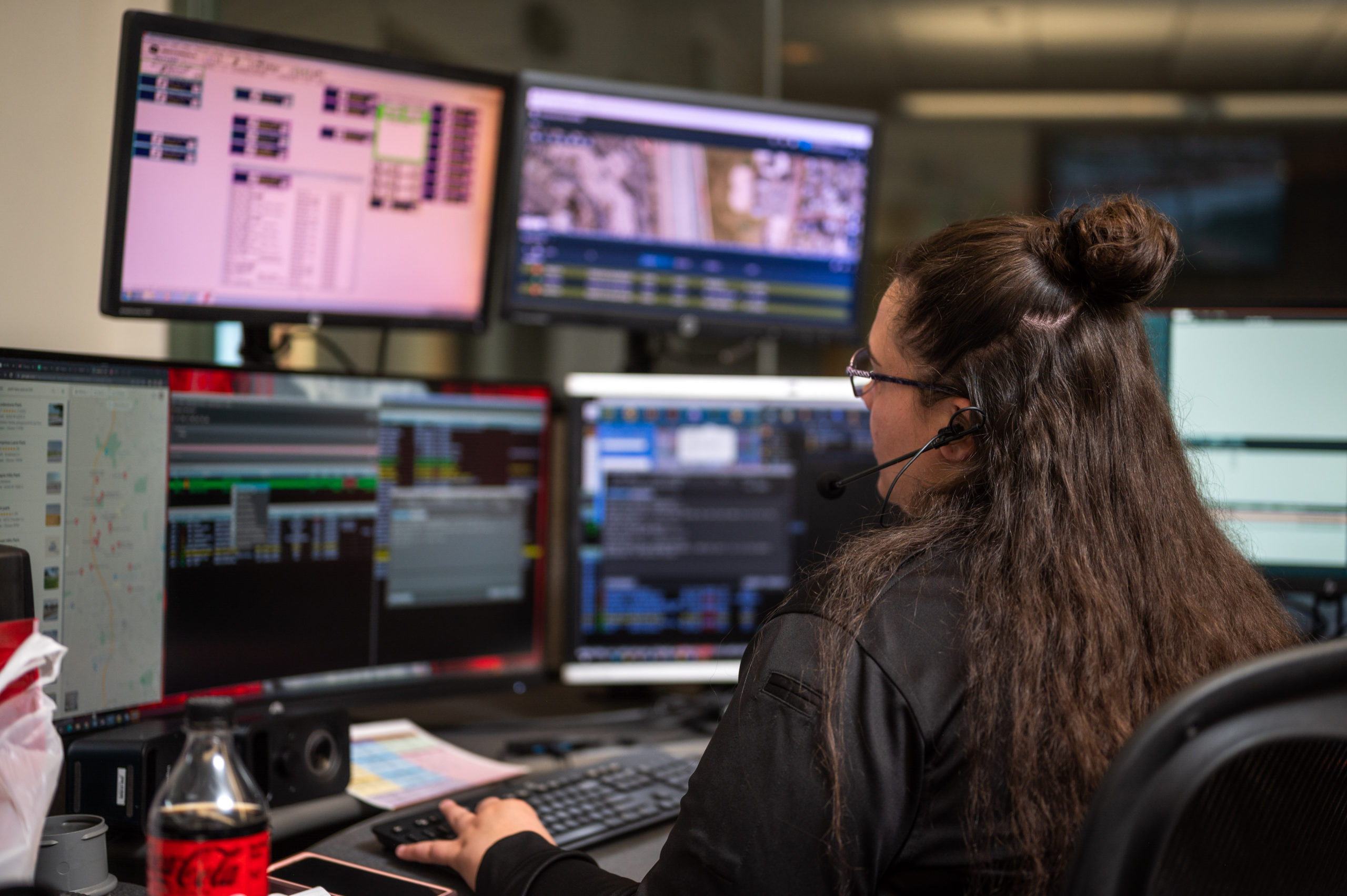A dispatcher sits at a computer looking at multiple screens.