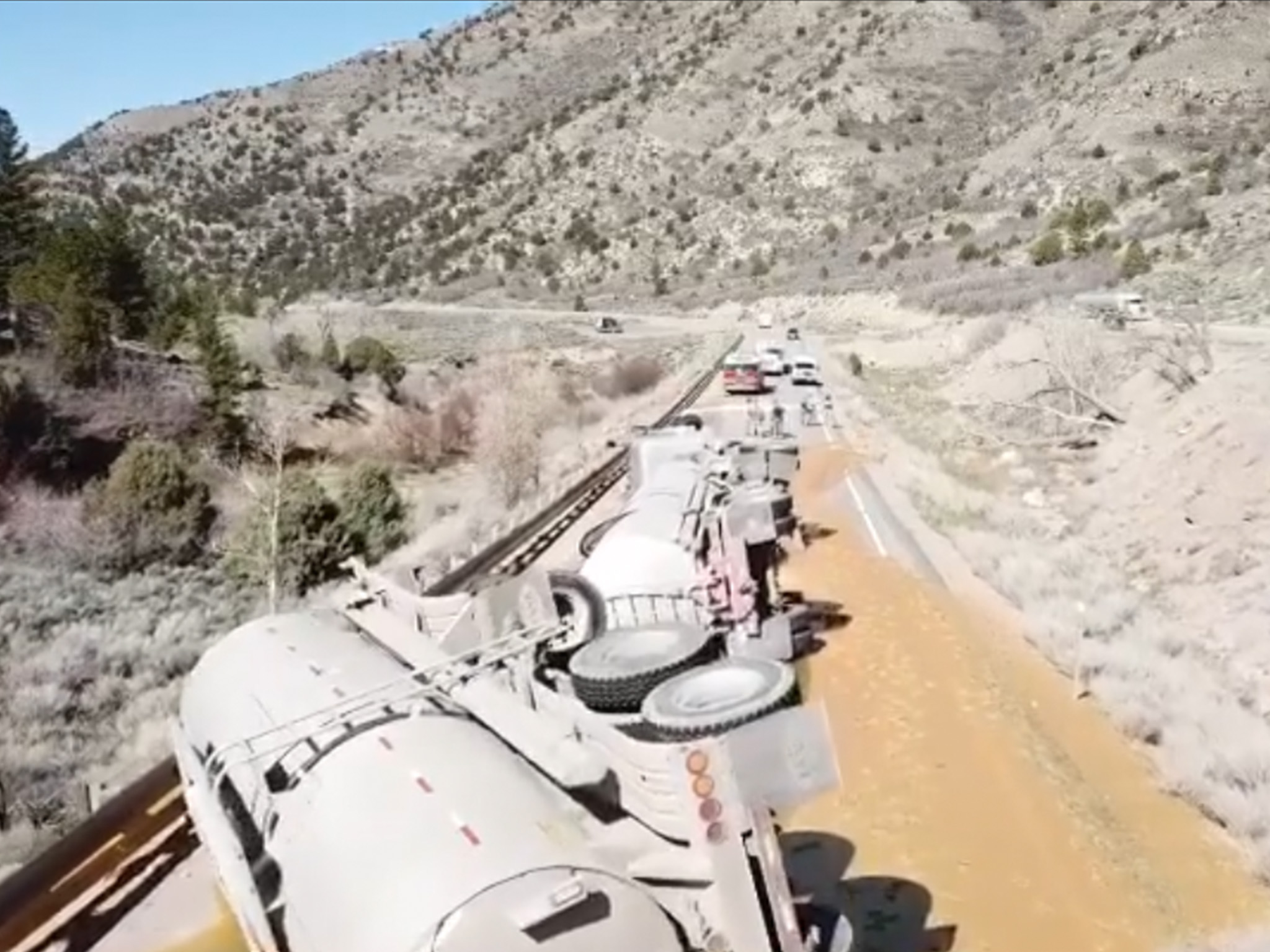 Drone photo shows aerial view of a tanker truck that tipped over on a roadway and is blocking all lanes.