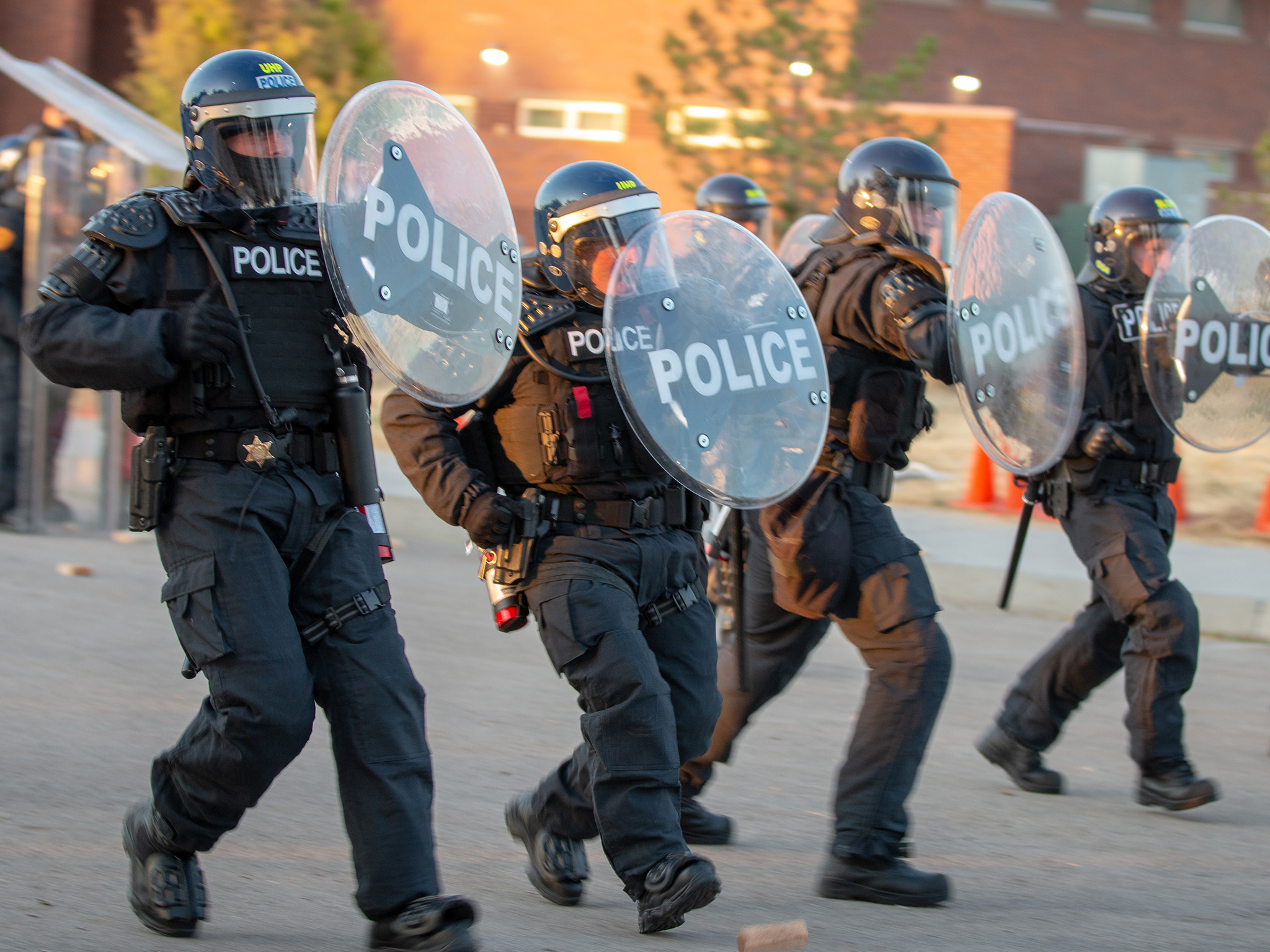 Four UHP Troopers are dressed in riot gear and holding shields that read "Police" and are participating in a PPU training exercise.