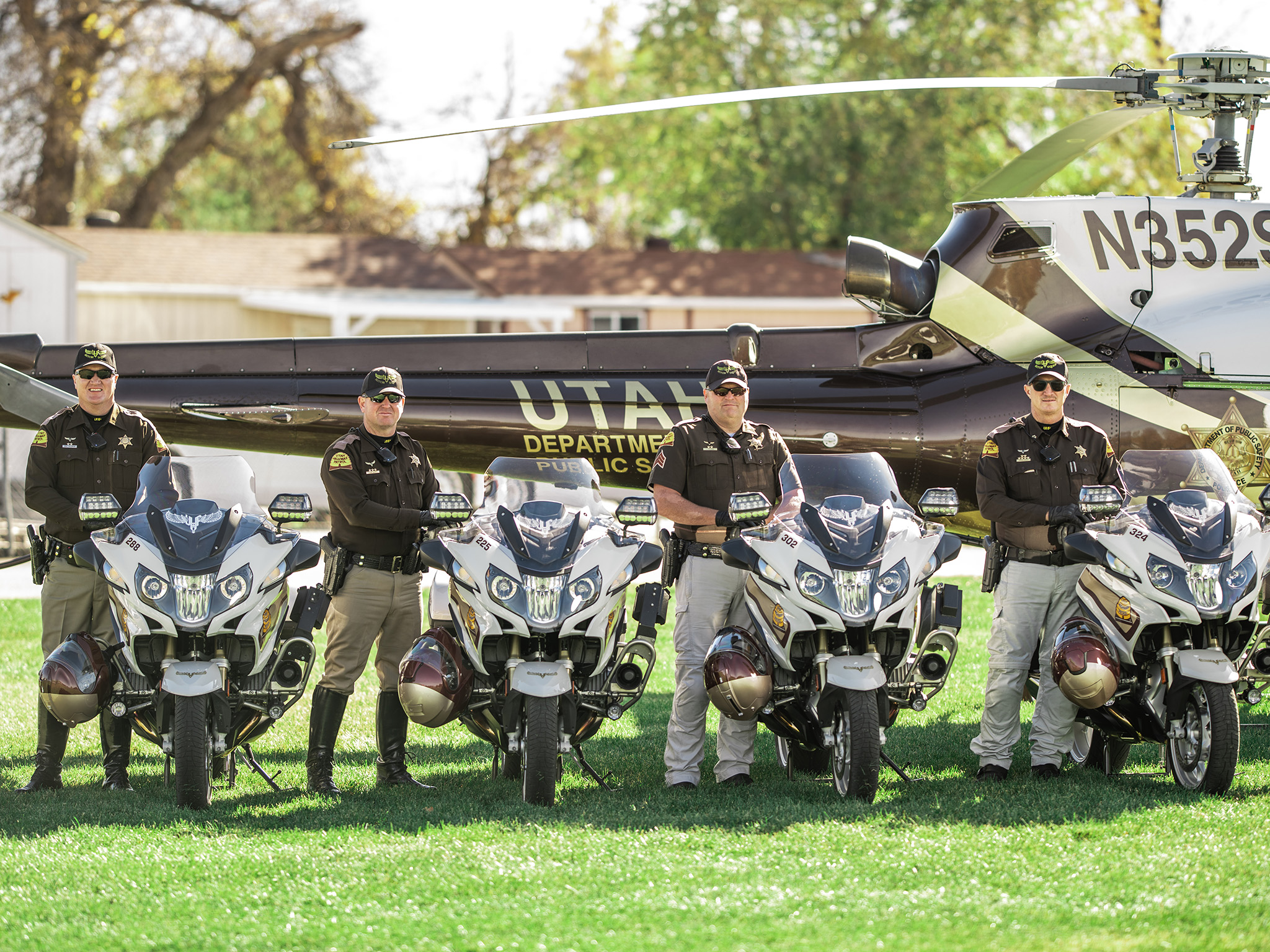 Four members of the motor squad stand by their motorcycles which are parked next to the helicopter/